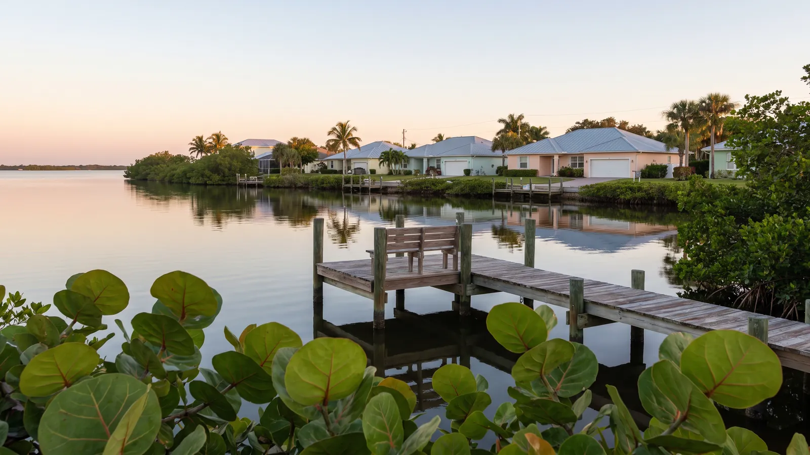 Waterfront homes with garages along the Indian River Lagoon near Jensen Beach, Florida, under a clear morning sky with sea grapes in the foreground